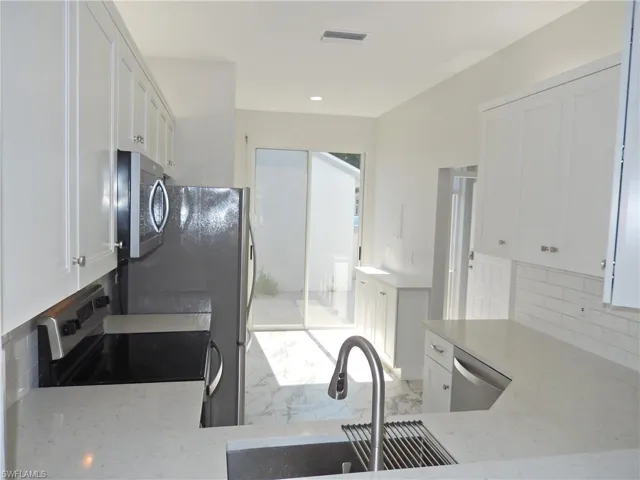 Kitchen with backsplash, appliances with stainless steel finishes, and white cabinets