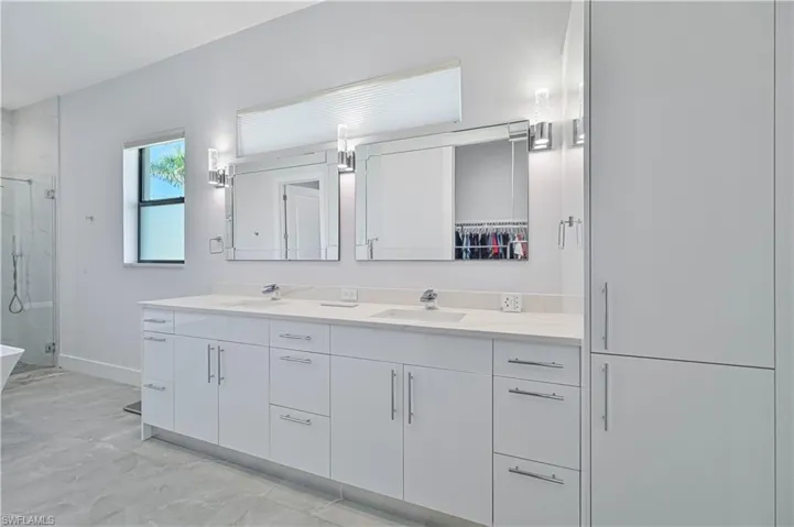 Full bath with a shower stall, double vanity, baseboards, and a sink