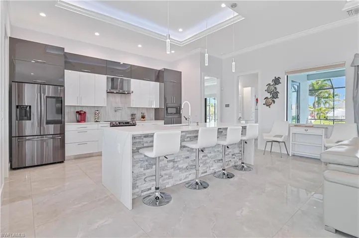 Kitchen featuring a kitchen bar, light countertops, stainless steel appliances, wall chimney exhaust hood, and modern cabinets