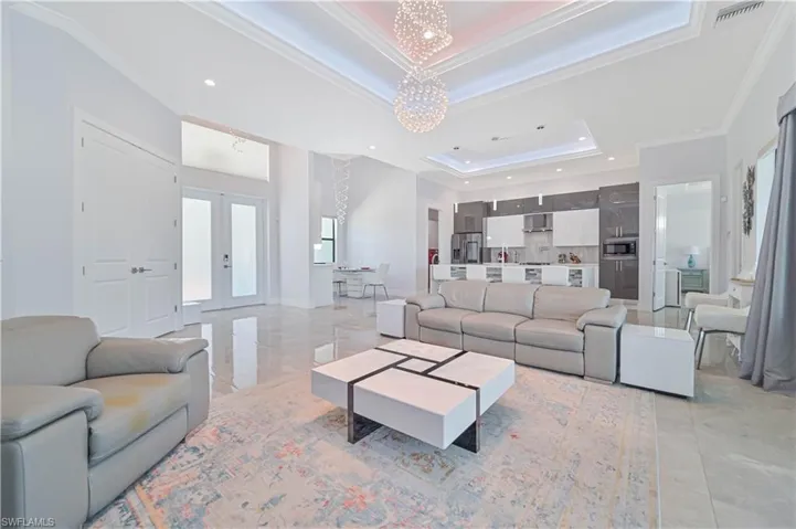 Living room with an inviting chandelier, a raised ceiling, crown molding, and french doors