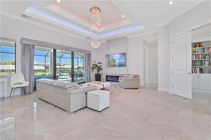 Living room with visible vents, a tray ceiling, a glass covered fireplace, crown molding, and a notable chandelier