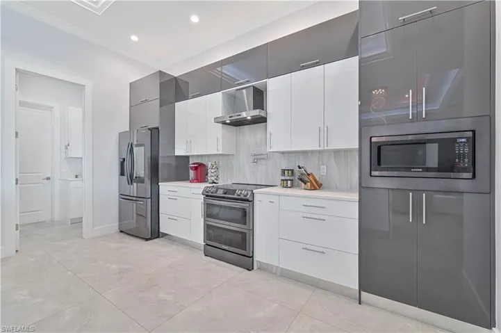Kitchen with appliances with stainless steel finishes, wall chimney exhaust hood, crown molding, light countertops, and decorative backsplash