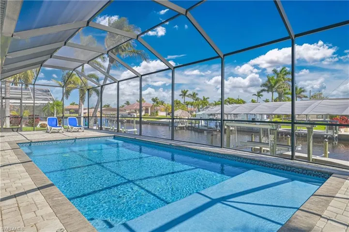 Outdoor pool featuring glass enclosure, a dock, a water view, a patio area, and a residential view