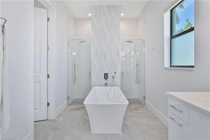 Bathroom featuring a marble finish shower, a soaking tub, vanity, and baseboards