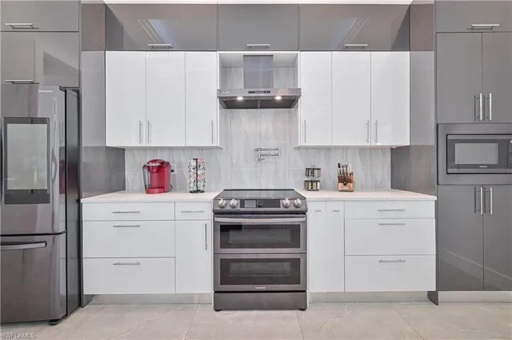 Kitchen featuring stainless steel appliances, wall chimney exhaust hood, decorative backsplash, and light countertops