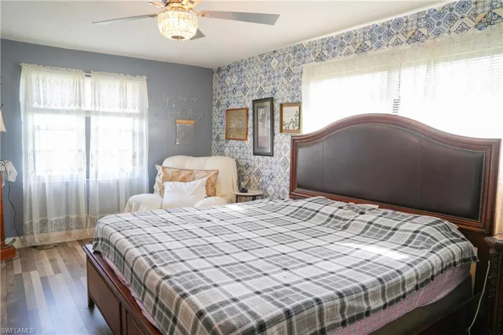 Bedroom featuring a detailed wood-finish headboard, patterned accent wall, wood-finish flooring, and a decorative ceiling fan