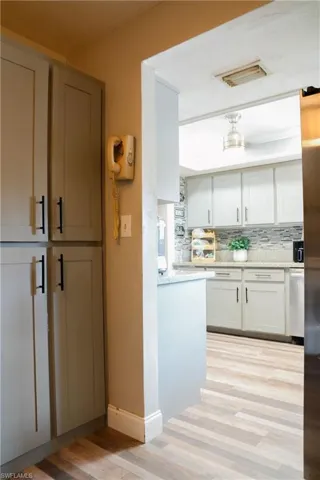 Kitchen featuring light gray cabinetry with black hardware, wood-finish flooring, a light-toned countertop, and a gray tile backsplash