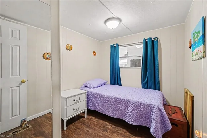 Panel-style wall covering, wood-finish flooring, and a single window with curtain rods