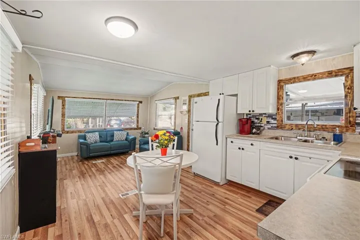 Open-concept living space with wood-finish flooring, white cabinetry, a tiled backsplash, and recessed lighting