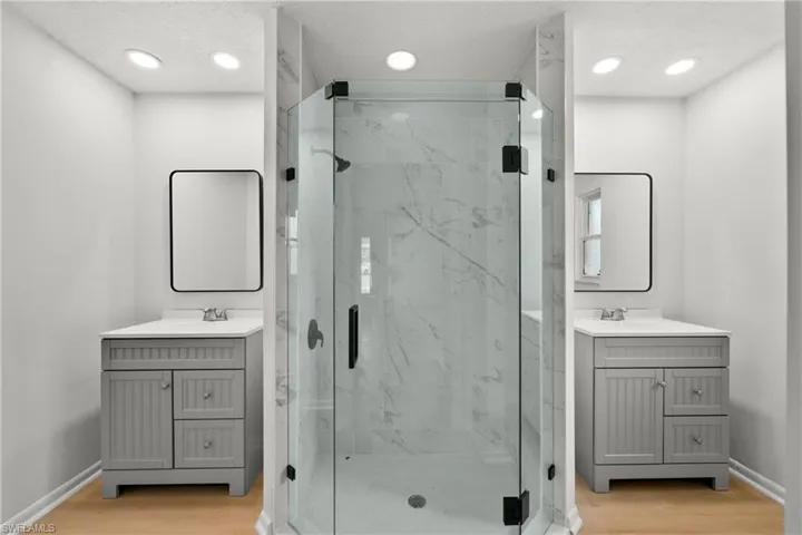 Bathroom featuring dual sinks, vanity with extensive cabinet space, a shower with shower door, and hardwood / wood-style flooring
