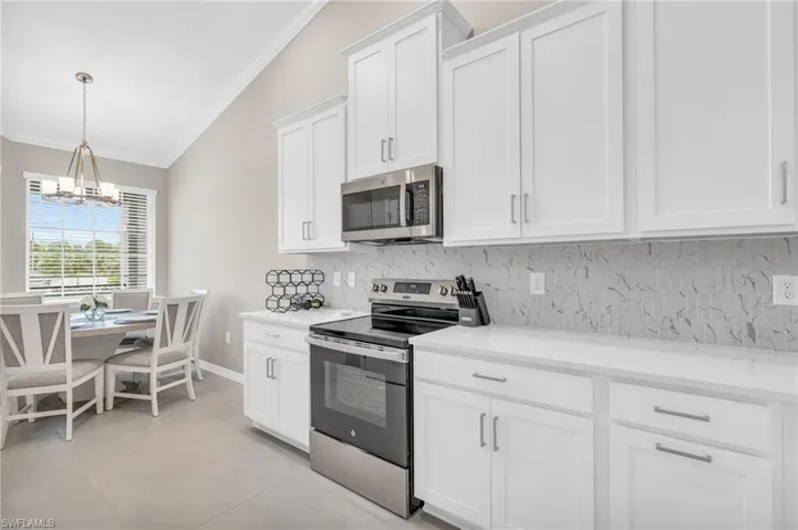 Kitchen featuring lofted ceiling, decorative backsplash, light tile patterned floors, appliances with stainless steel finishes, and white cabinets