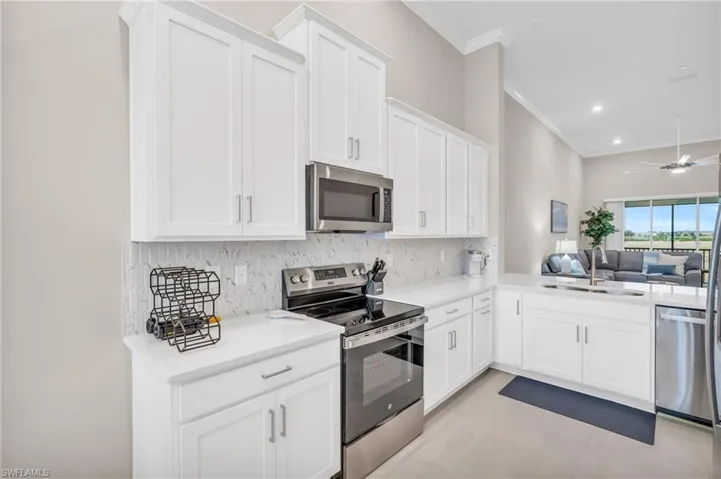 Kitchen with appliances with stainless steel finishes, white cabinets, backsplash, and sink