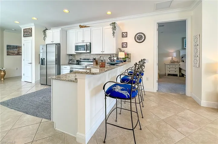 Kitchen featuring a kitchen breakfast bar, light stone countertops, stainless steel appliances, backsplash, and light tile floors