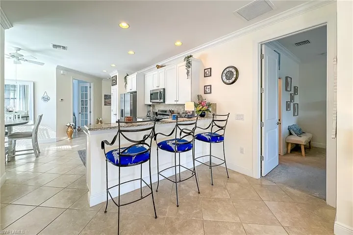 Kitchen with a kitchen breakfast bar, kitchen peninsula, stainless steel appliances, light tile flooring, and white cabinets