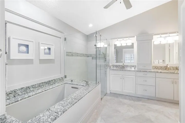 Bathroom featuring lofted ceiling, plus walk in shower, vanity, a textured ceiling, and ceiling fan