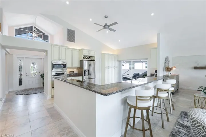 Kitchen with a kitchen breakfast bar, stainless steel appliances, dark stone counters, high vaulted ceiling, and ceiling fan