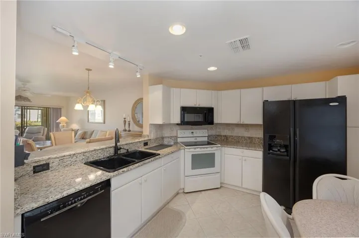 Kitchen with black appliances, white cabinets, open floor plan, light stone countertops, and light tile patterned floors