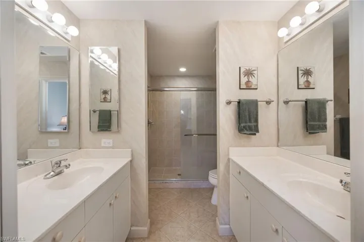 Bathroom featuring two vanities, a stall shower, and light tile patterned flooring