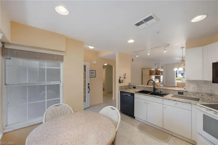 Kitchen with arched walkways, black appliances, white cabinetry, light stone countertops, and decorative backsplash