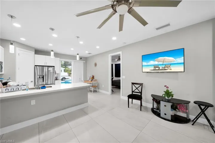Kitchen with stainless steel fridge with ice dispenser, white cabinets, pendant lighting, ceiling fan, and light stone counters