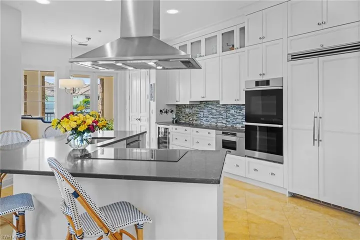 Kitchen featuring decorative backsplash, island exhaust hood, a breakfast bar area, dark stone countertops, and recessed lighting