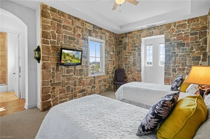 Carpeted bedroom featuring multiple windows, arched walkways, and a ceiling fan