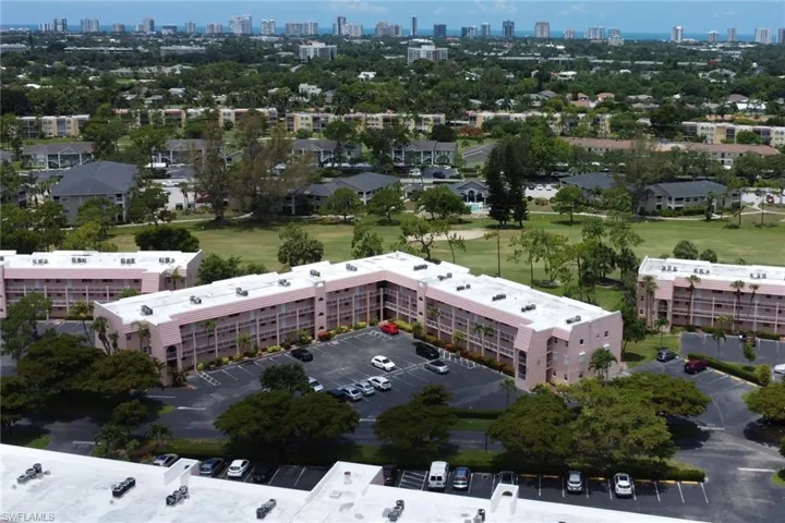 Expansive residential complex featuring multiple buildings with private balconies, ample surface parking, surrounded by mature trees and manicured green spaces