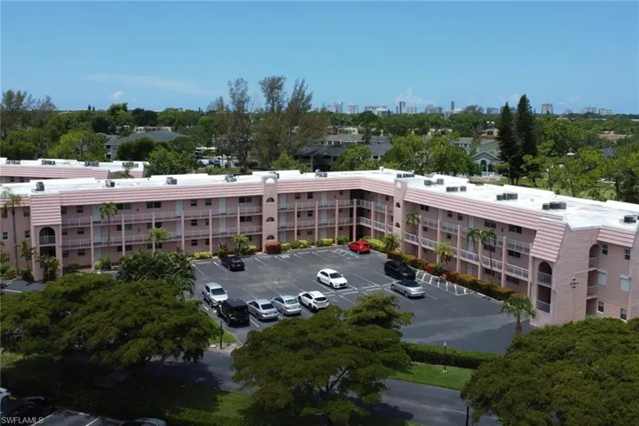 Multi-story residential building featuring private balconies, an exterior parking lot, and mature landscaping