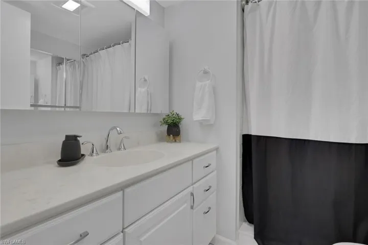 Bathroom vanity featuring a white countertop with an integrated sink, chrome faucet, white cabinetry, and an overhead mirrored medicine cabinet