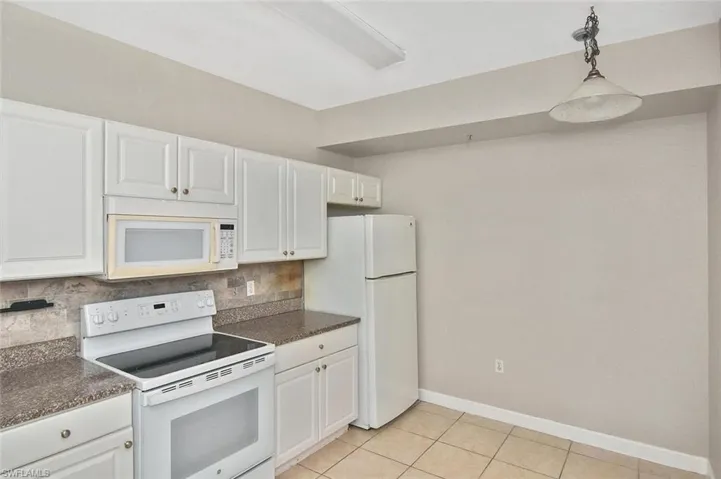 Kitchen with white appliances, hanging light fixtures, white cabinets, backsplash, and light tile patterned flooring