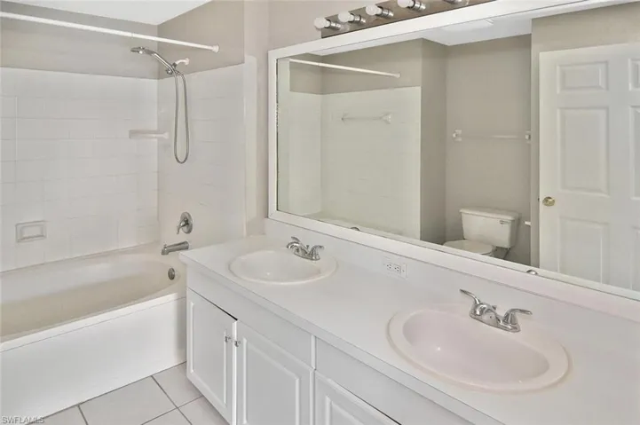 Bathroom with double vanity, washtub / shower combination, and light tile patterned flooring
