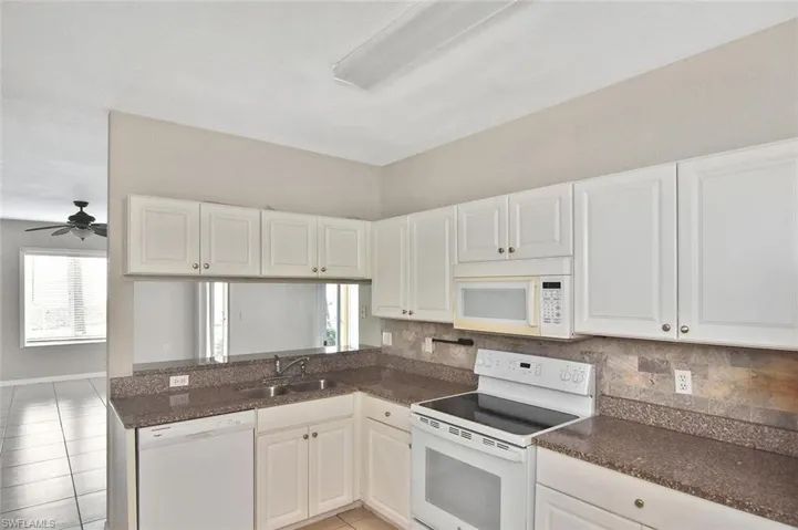 Kitchen featuring white appliances, ceiling fan, white cabinets, and backsplash