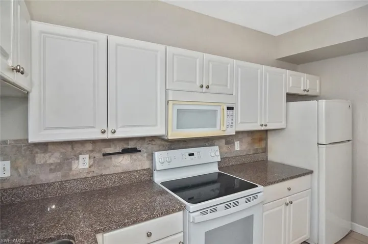 Kitchen with white appliances, tasteful backsplash, white cabinetry, and dark stone countertops