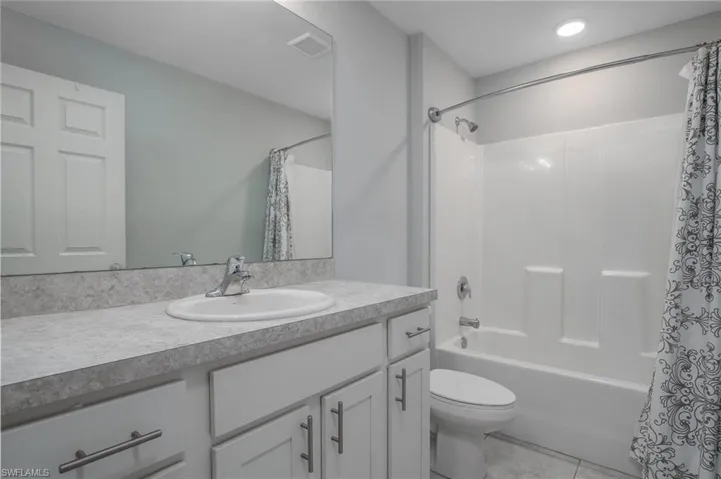 Full bath featuring tile patterned floors, shower / bath combo, toilet, vanity, and visible vents