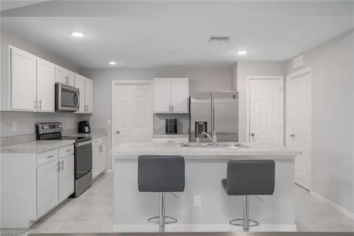 Kitchen featuring stainless steel appliances, a kitchen bar, a sink, visible vents, and a center island with sink