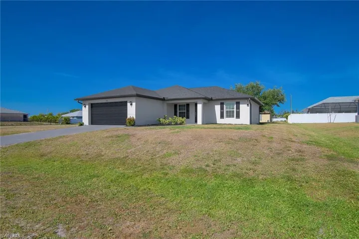 View of front of house with a front lawn, a garage, driveway, stucco siding, and fence