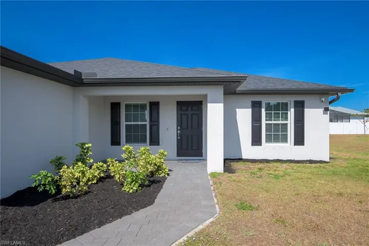 Doorway to property with stucco siding, roof with shingles, covered porch, and a yard