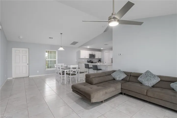 Living area with light tile patterned floors, baseboards, visible vents, a ceiling fan, and high vaulted ceiling