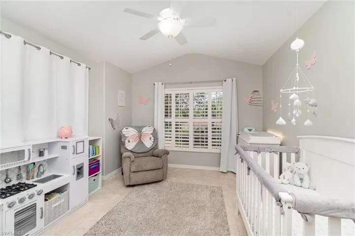 Bedroom featuring vaulted ceiling, light tile patterned floors, a nursery area, a ceiling fan, and baseboards