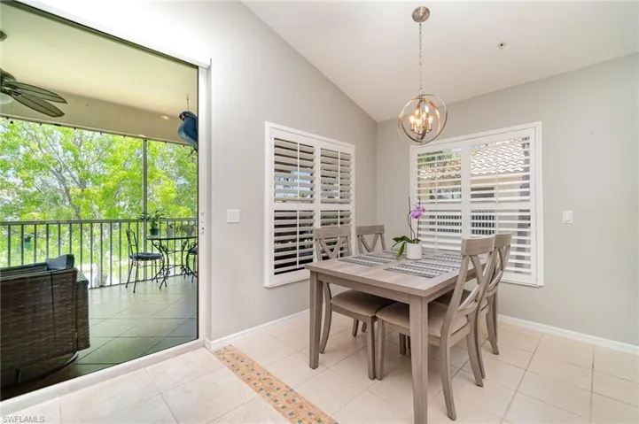 Dining area with lofted ceiling, light tile patterned floors, a chandelier, baseboards, and a ceiling fan