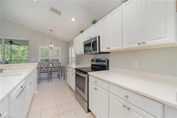 Kitchen with appliances with stainless steel finishes, a sink, lofted ceiling, light tile patterned floors, and white cabinets
