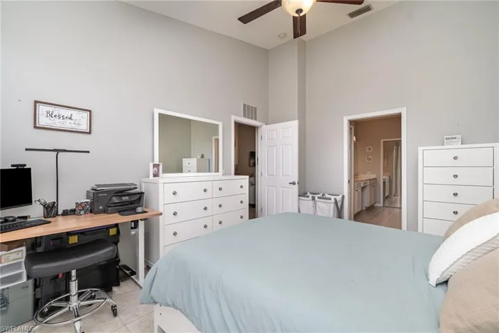 Bedroom featuring high vaulted ceiling, light tile patterned floors, an office area, ensuite bath, and a ceiling fan