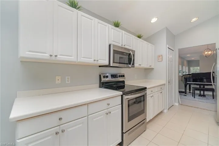 Kitchen with appliances with stainless steel finishes, white cabinetry, light tile patterned floors, recessed lighting, and lofted ceiling
