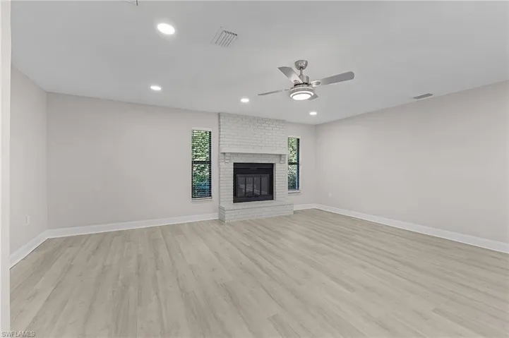 Unfurnished living room with a brick fireplace, ceiling fan, and light wood-type flooring