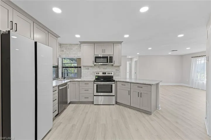 Kitchen featuring gray cabinetry, light stone counters, stainless steel appliances, and light hardwood / wood-style flooring