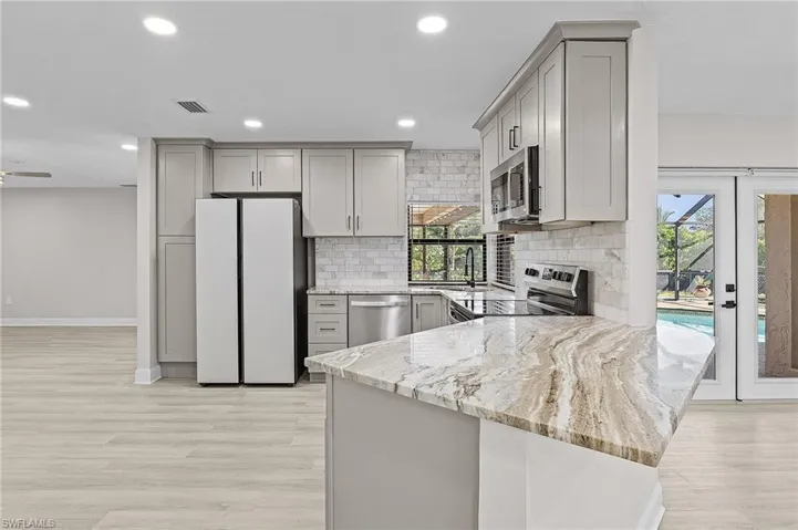 Kitchen featuring kitchen peninsula, appliances with stainless steel finishes, light stone counters, and gray cabinetry