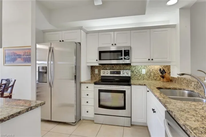 Kitchen featuring light stone countertops, stainless steel appliances, tasteful backsplash, and white cabinetry