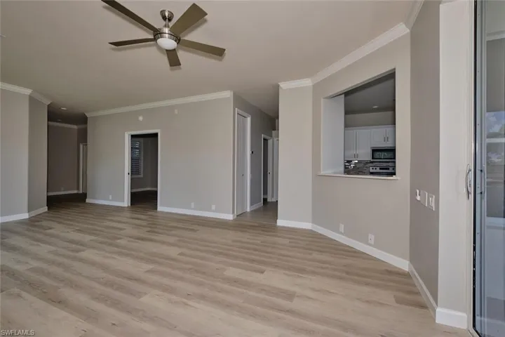 Unfurnished living room with crown molding, light wood-style floors, and ceiling fan