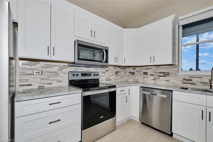 Kitchen featuring stainless steel appliances, white cabinetry, light stone countertops, and backsplash