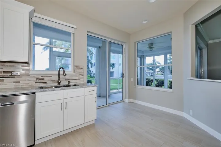 Kitchen featuring stainless steel dishwasher, light stone counters, white cabinets, crown molding, and tasteful backsplash